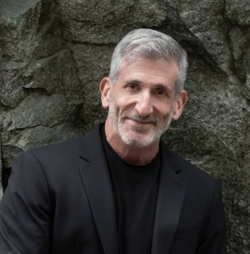 Senior mycologist with gray hair and beard standing outdoors near rocks.